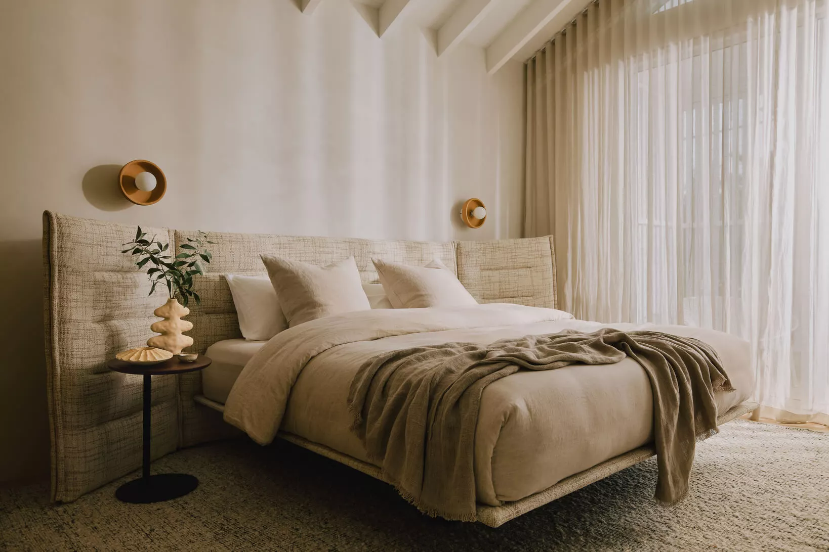 A softly lit bedroom in the evening with a book, a warm lamp, and neatly arranged bedding
